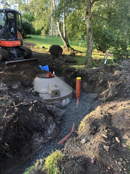 Nedgrävd tank för minireningsverk i ett schakt med grus och rör, grävmaskin bakom.